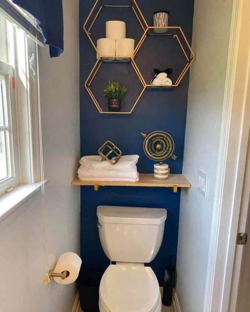 Navy blue accent wall with gold hexagonal shelves and a white toilet in a small bathroom.