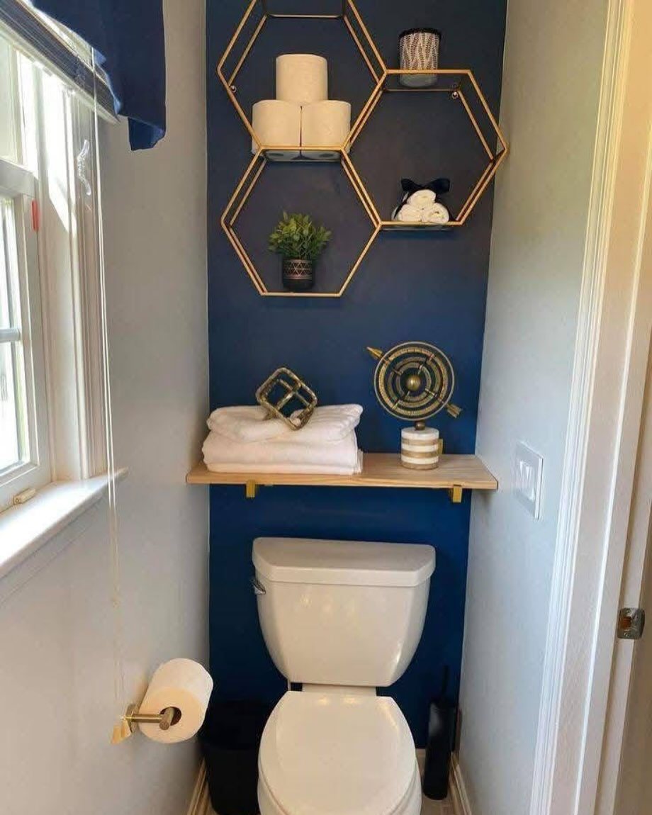 Navy blue accent wall with gold hexagonal shelves and a white toilet in a small bathroom.