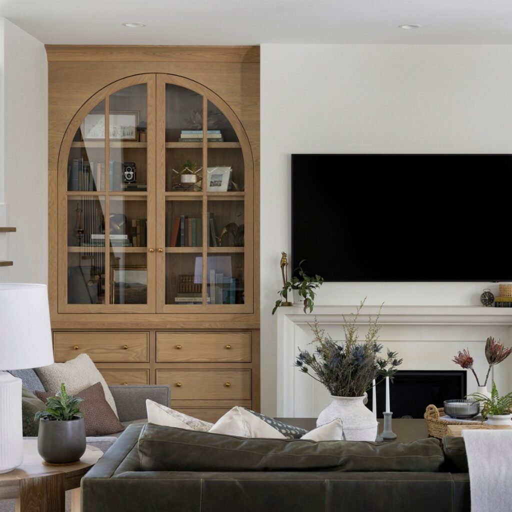 Light wood built-in unit with arched glass doors and bottom drawers in a living room.