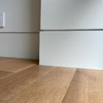 White baseboard moulding meeting a white wall and light wood plank flooring in a corner.