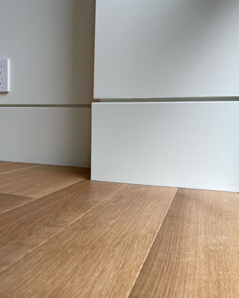 White baseboard moulding meeting a white wall and light wood plank flooring in a corner.