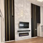 Black vertical slat wall panels with gold accents flanking a white marble fireplace and television wall.
