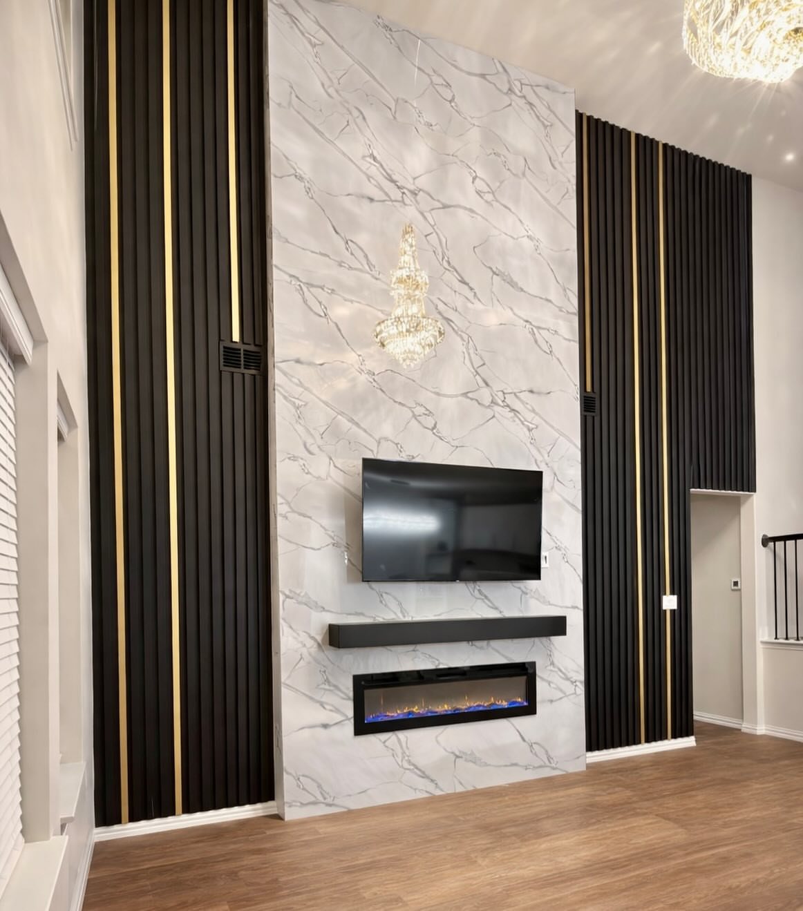 Black vertical slat wall panels with gold accents flanking a white marble fireplace and television wall.