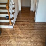 Warm brown hardwood flooring runs through a hallway next to a set of wooden stairs.