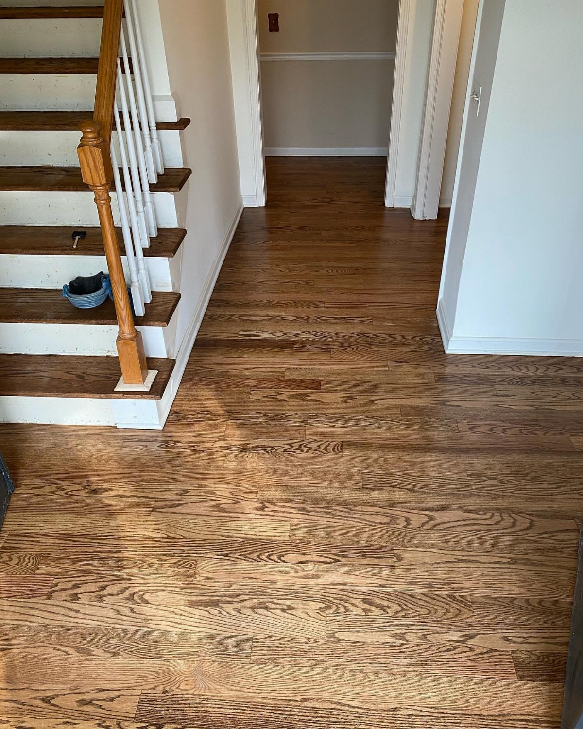 Warm brown hardwood flooring runs through a hallway next to a set of wooden stairs.
