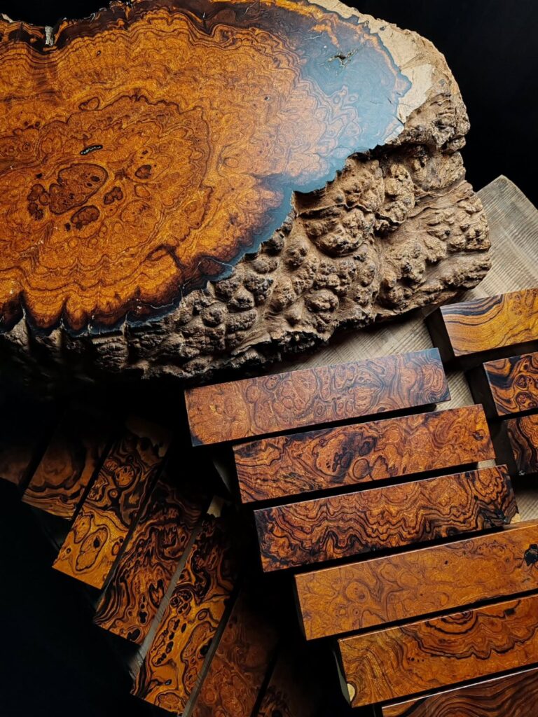 Swirling burl wood slab and rectangular wooden blocks with intricate, dark grain patterns on a dark background.