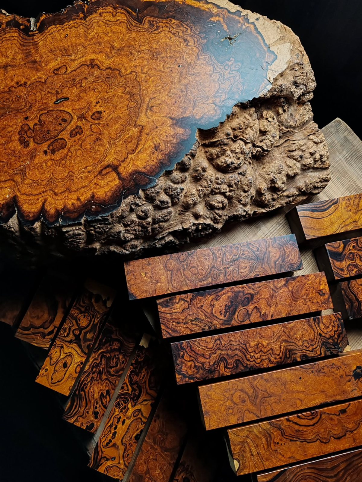 Swirling burl wood slab and rectangular wooden blocks with intricate, dark grain patterns on a dark background.